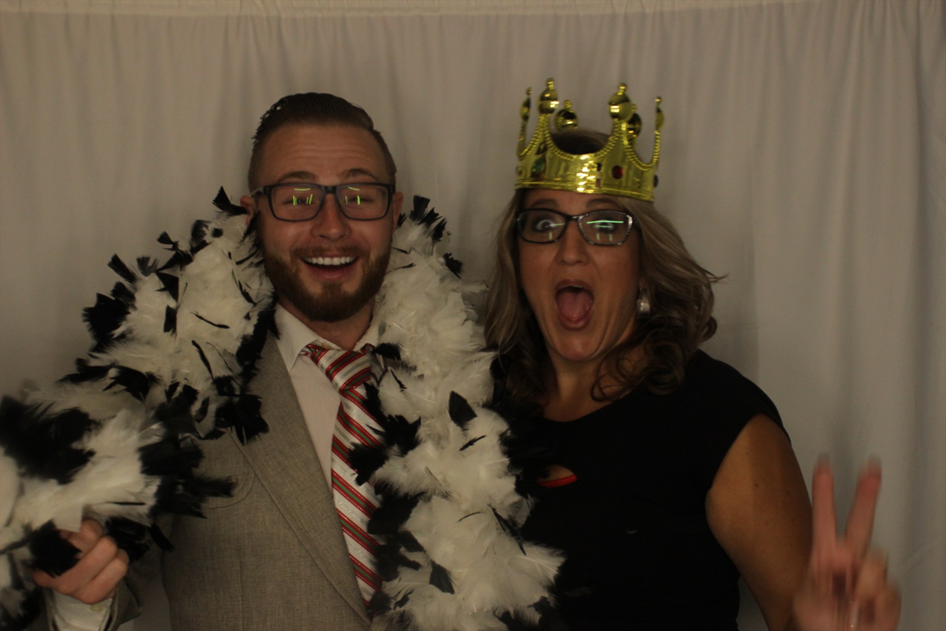 Two party guests laughing in a crown, glasses, and feather boas