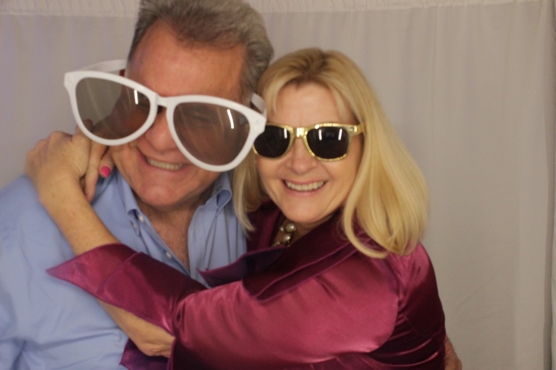 A smiling couple wearing oversized sunglasses at the photo booth