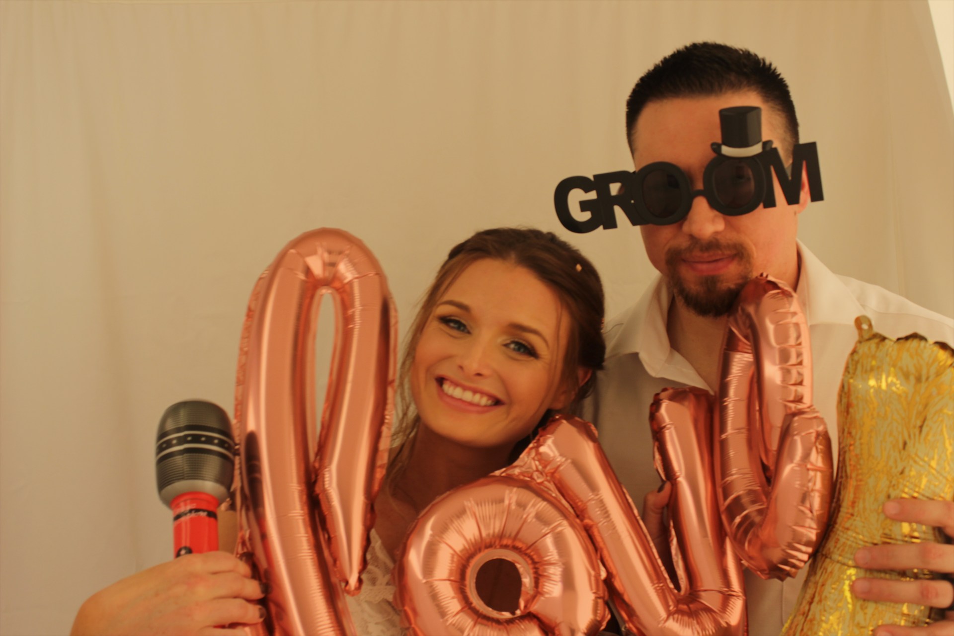 A couple posing with wedding props, a toy microphone, and metallic balloon letters