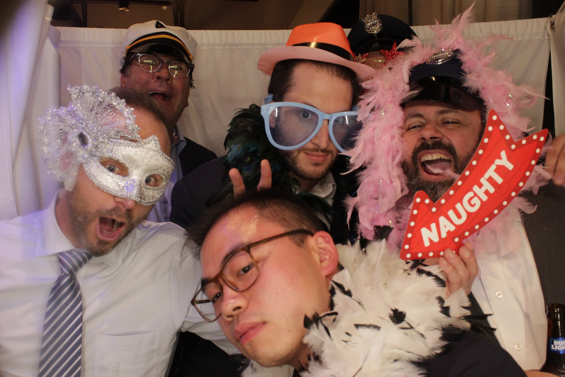 Five guests crowding into the photo booth with hats, glasses, masks, and boas