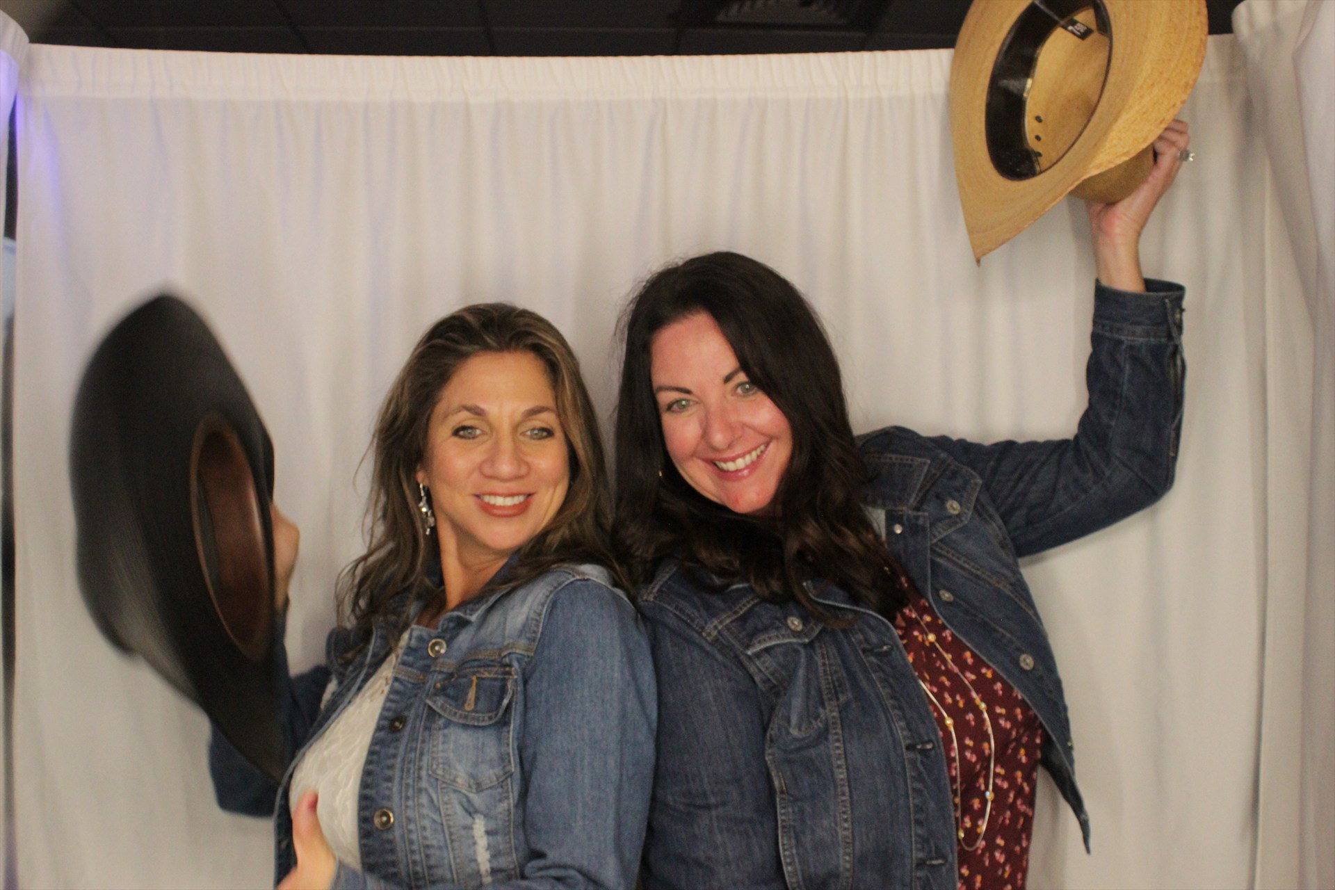 Two smiling women posing back-to-back with cowboy hats
