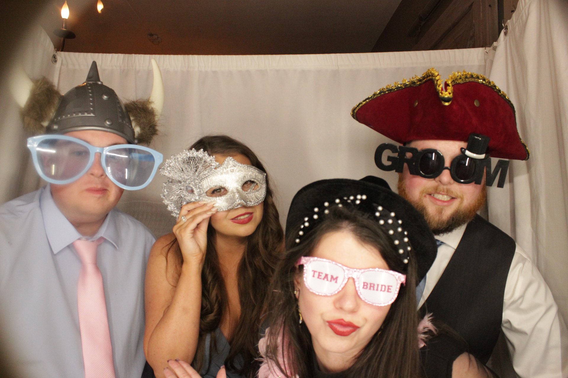 Four wedding guests posing with oversized glasses, hats, and a masquerade mask