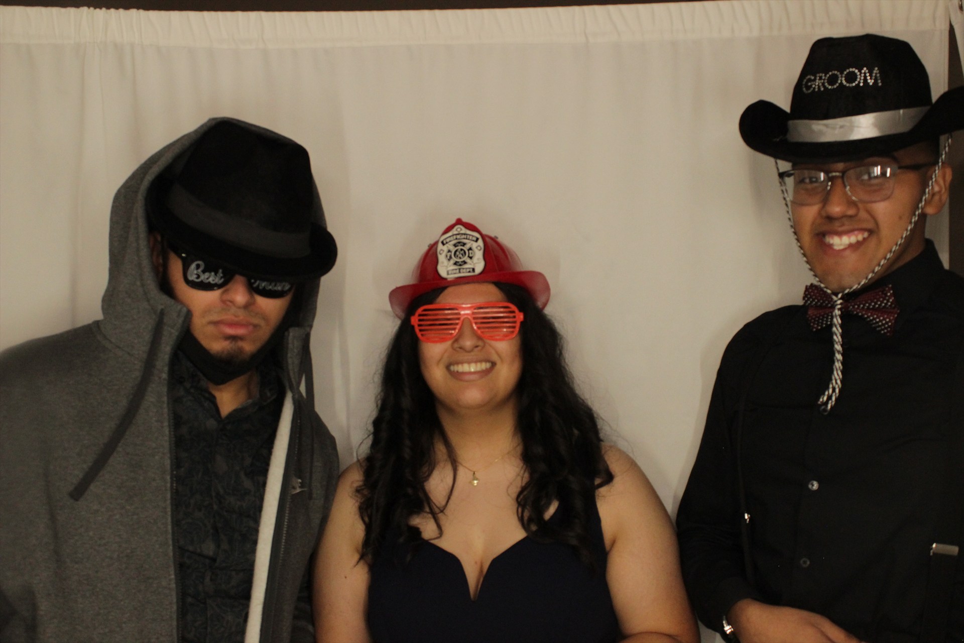 Three guests posing with playful hats, glasses, and a bow tie