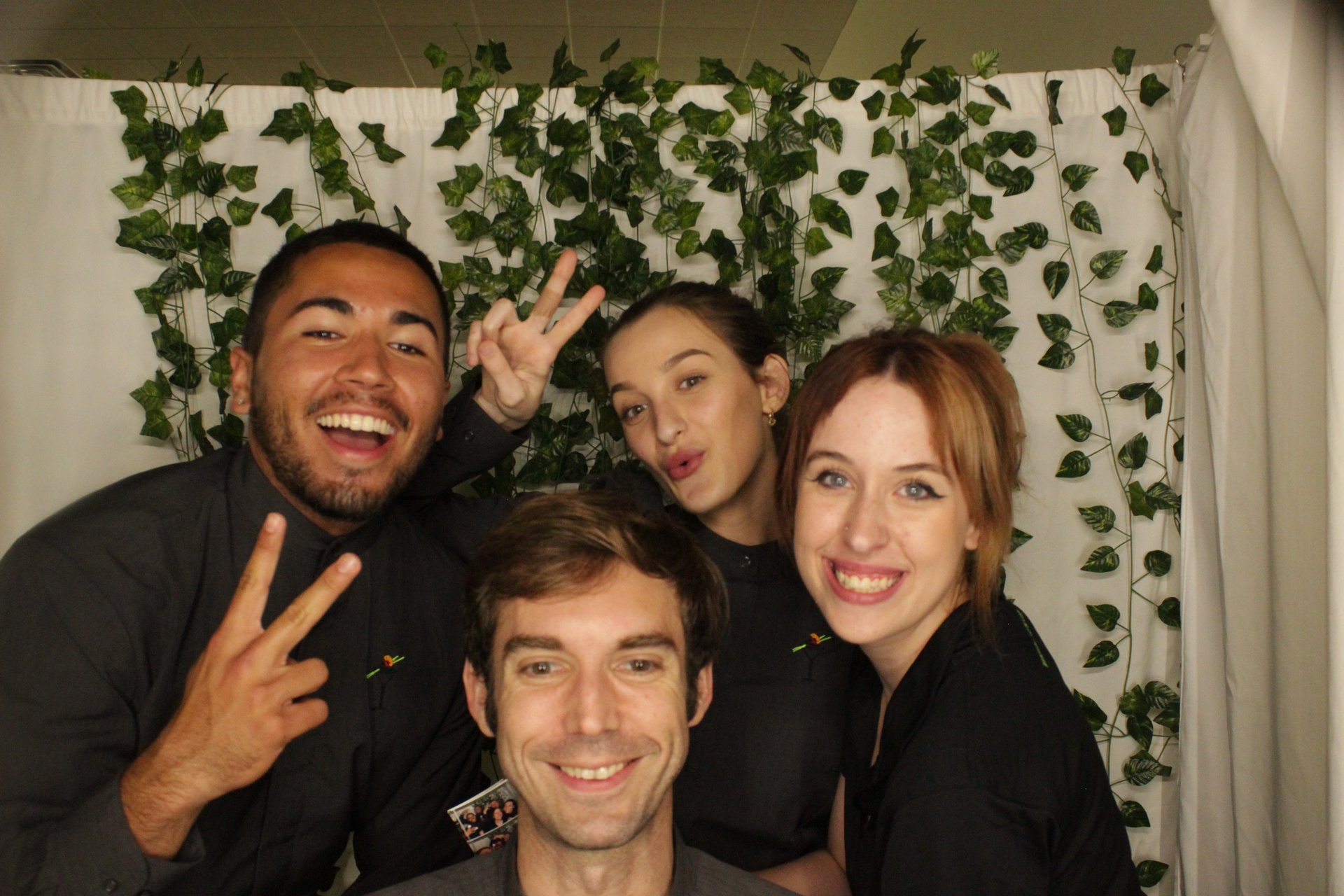 Four smiling guests gathered in front of a leafy photo booth backdrop