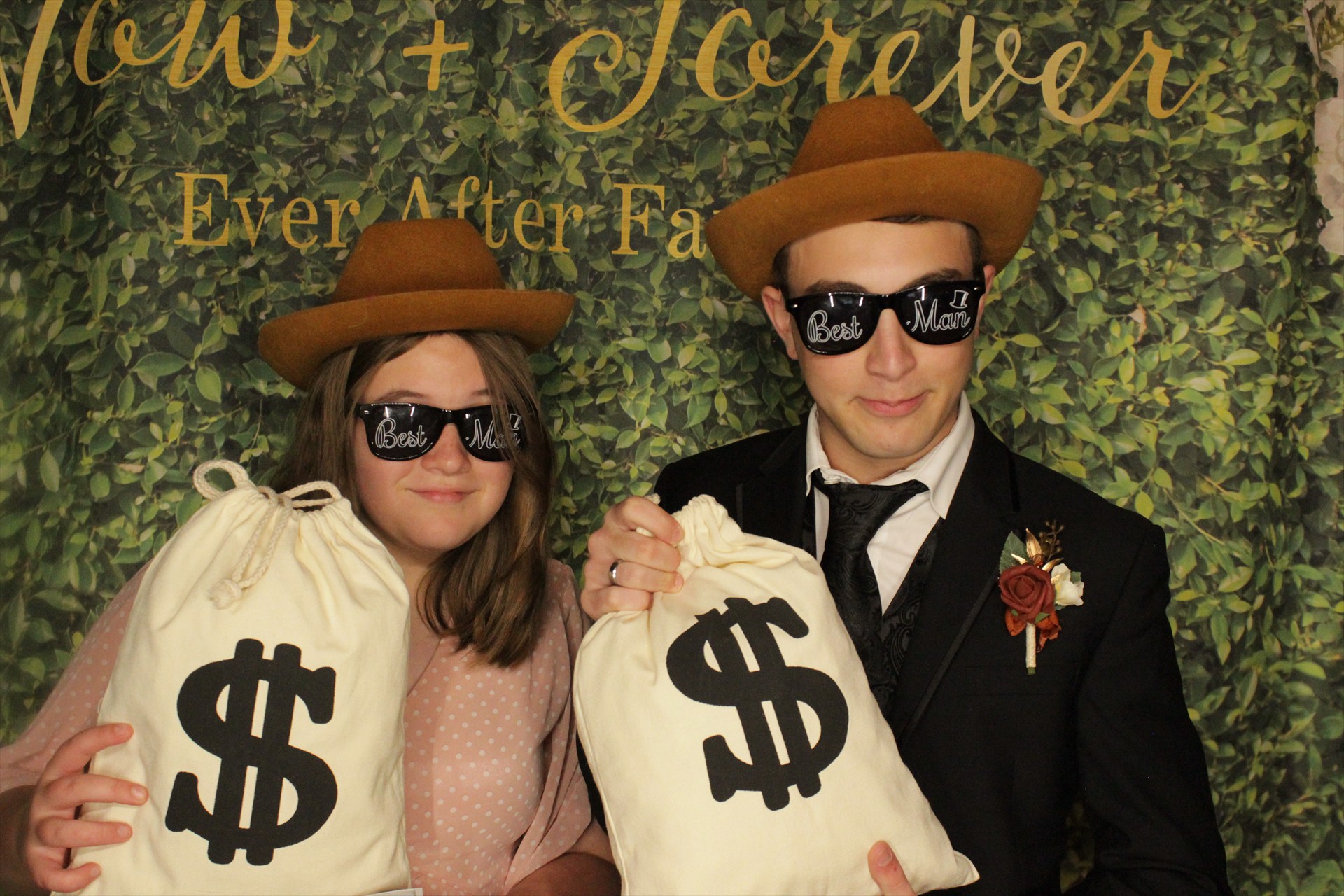 Two wedding guests wearing cowboy hats and novelty sunglasses while holding money bag props