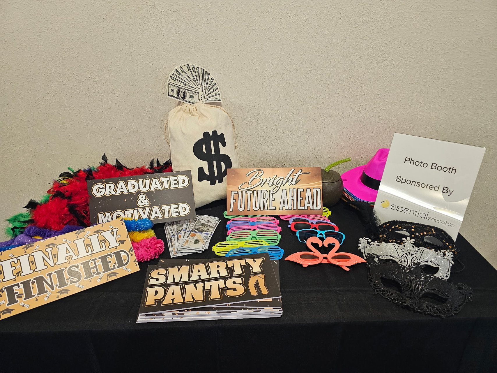A graduation photo booth prop table with signs, glasses, masks, hats, and money props
